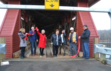 A group of individuals cut a red ribbon in front of a red covered bridge.