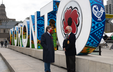 Two men standing in front of a colourful sign spelling out the word, Toronto.