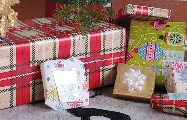 Wrapped presents under a Christmas tree. There is one large box wrapped in plaid wrapping paper and six smaller presents wrapped in various kinds of paper.