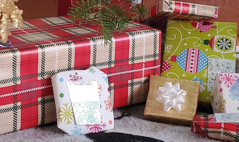 Wrapped presents under a Christmas tree. There is one large box wrapped in plaid wrapping paper and six smaller presents wrapped in various kinds of paper.