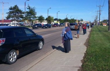 People line the sidewalk holding signs.