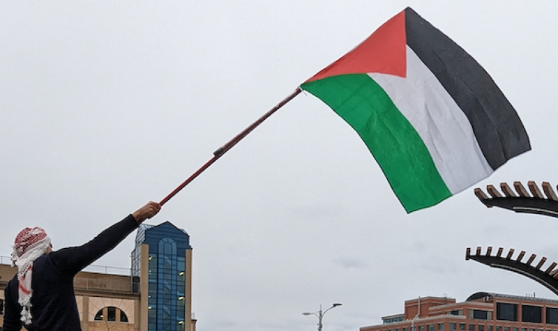A man wearing the kaffiyeh waves a large Palestinian flag over the crowd gathered in Uptown Waterloo to show support for the Palestine territories