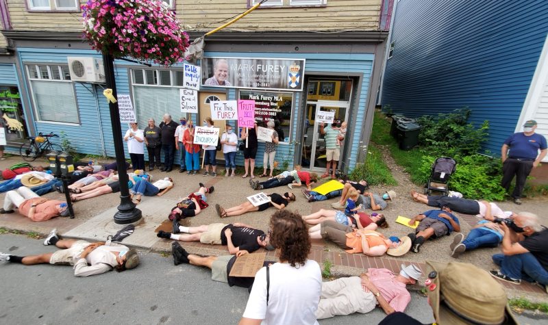 Protesters calling for a public inquiry into the April mass shooting lie on the sidewalk in front of Justice Minister Mark Furey's office to represent the 22 people killed