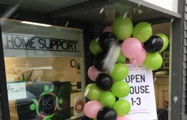 Balloons and signs in a window announce an open house at Queens County Home Support.