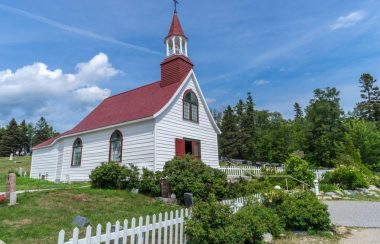 Une chapelle blanche avec un toit rouge bordée de plante