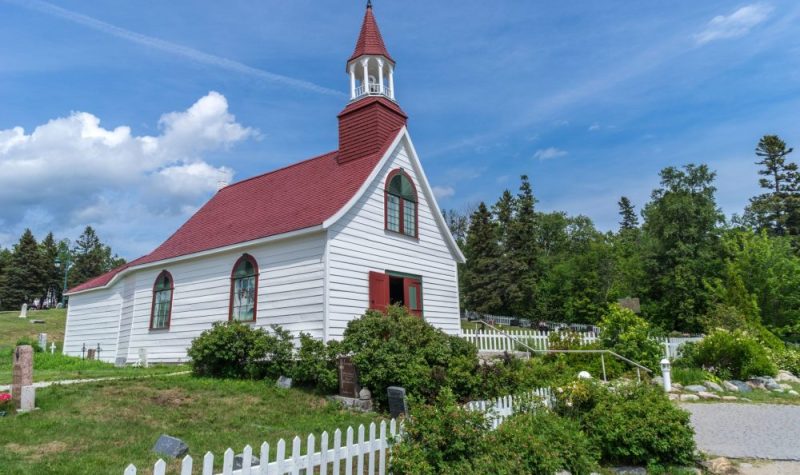 Une chapelle blanche avec un toit rouge bordée de plante