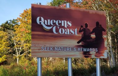 Road sign showing two people in a canoe with the words Queens Coast