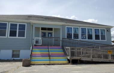 The outside of Queens County Daycare on a sunny day. The building has rainbow steps.