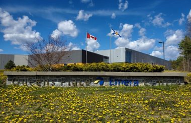 A low rise building against a blue sky and a sign reading 'Queens Place Emera Centre' and Canadian and Nova Scotia flag.