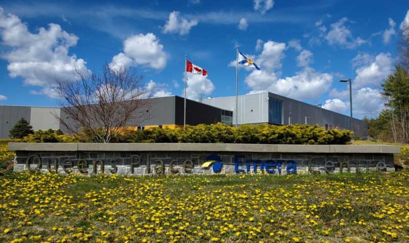 A low rise building against a blue sky and a sign reading 'Queens Place Emera Centre' and Canadian and Nova Scotia flag.