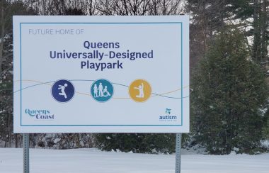 A sign in front of a snowy stand of trees indicates a playground is to be built in that location