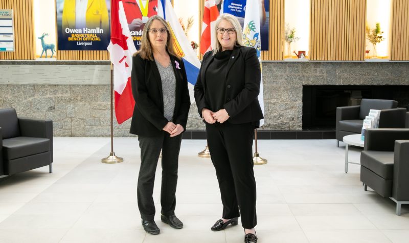 Two women stand in front of a row of flags inside a recreation facility