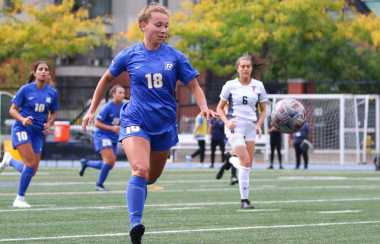 Soccer players with white and blue jerseys play on a green field outdoors.