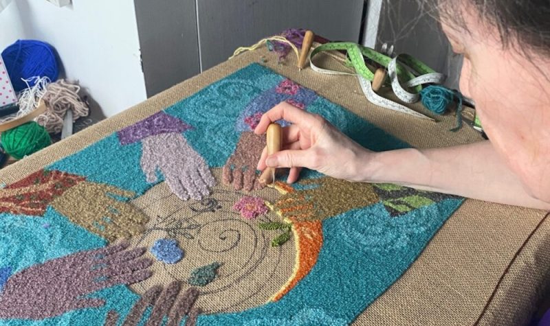 Dame travaillant sur un tapis en laine représentant des mains disposées en cercle.