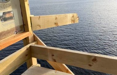 A broken wooden rail hangs off a bridge over a river