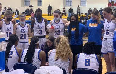 People in white basketball jerseys in a close huddle on a team bench.