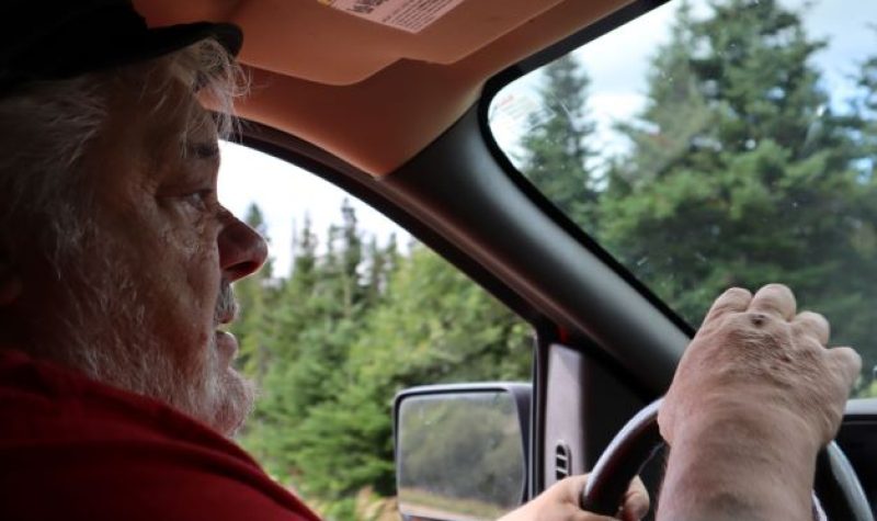 Le maire et préfet Randy Jones est photographié à bord de sa camionnette. Il porte un t-shirt rouge. En arrière-plan, on voit la forêt.