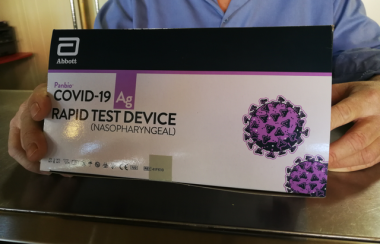 A close up of a white, black and purple COVID-19 rapid test kit box that someone is holding.