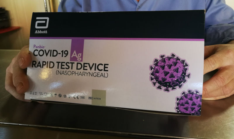 A close up of a white, black and purple COVID-19 rapid test kit box that someone is holding.