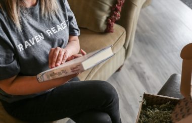 A woman reading a book with a shirt that says 'Raven Reads'