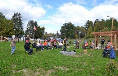 A group of people seated in lawn chairs around a fire, most wearing orange .