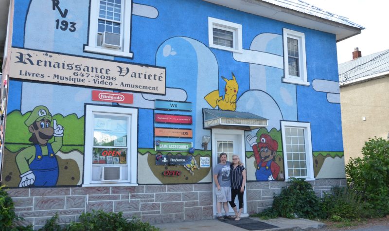 The Yerecks stand in the doorway of their business, which has a large Mario Brothers themed mural.