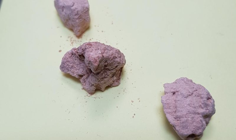 Three purple lumps made of a powderlike substance are pictured on a white background.