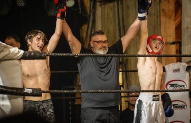 two teen boxers with fists in the air and a referee standing in the middle
