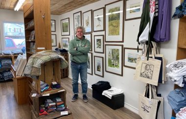 A man standing in a room with displays and lots of art handing on the walls.