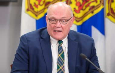 A man sits at a desk in front of a row of Nova Scotia flags