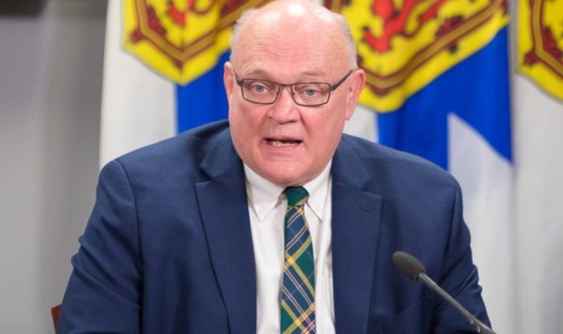 A man sits at a desk in front of a row of Nova Scotia flags