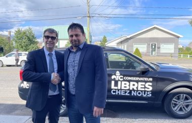 Deux hommes se serrant la main devant un véhicule sur lequel on peut voir le logo du Parti conservateur du Québec avec l'inscription : Libres chez nous.