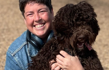 A person wearing a denim jacket smiles as they hold a dog.