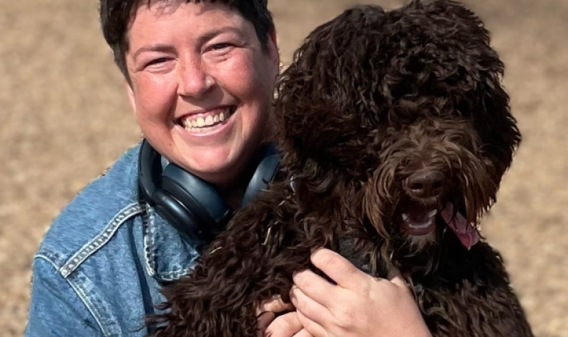 A person wearing a denim jacket smiles as they hold a dog.