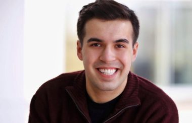 A young man smiling for the camera with a blurred background.