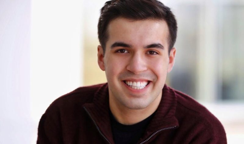 A young man smiling for the camera with a blurred background.