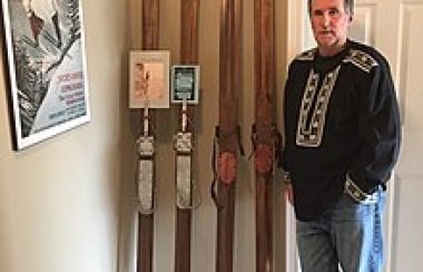 A man standing in a room beside four wooden pillars.