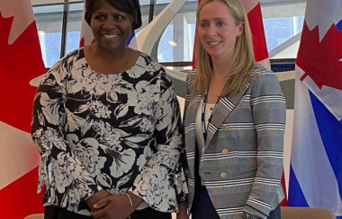 Two people in patterned shirts stand in front Canadian and Ontario flags.