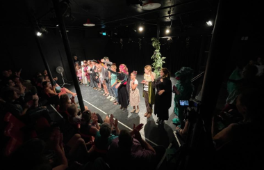 A group of kids in a variety of costumes on stage at the end of their performance