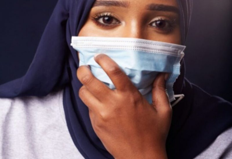 A young woman in a hijab holding a mask to her face