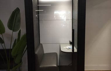 An office pod inside a room, the pod includes a couch with a table.