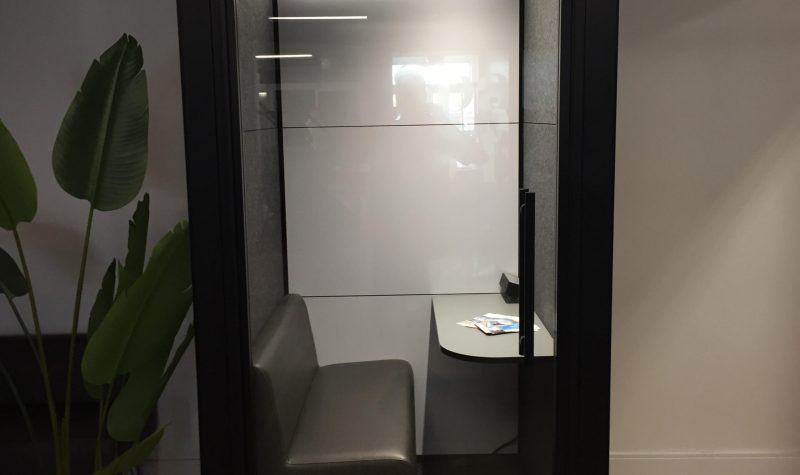 An office pod inside a room, the pod includes a couch with a table.