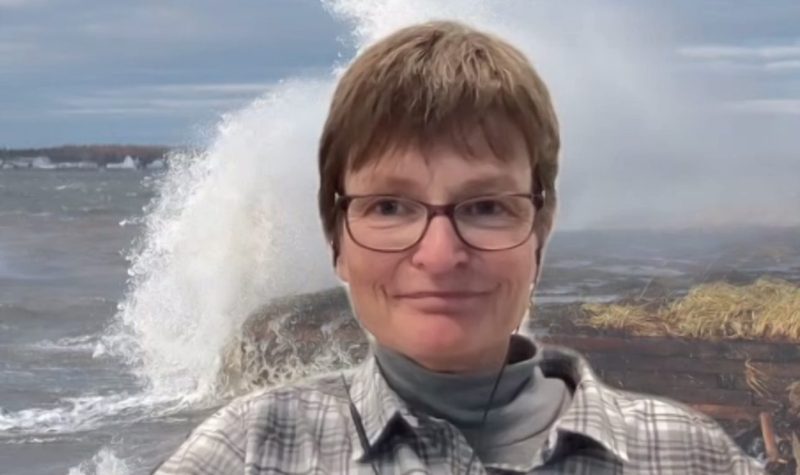 A woman with short dark hair and glasses is shown against a background image of a wave crashing onto the shore.