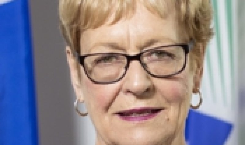 A professional headshot of Shawville Mayor Sandra Murray, wearing a purple shirt and glasses, standing in front of a Quebec flag.