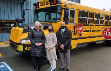 Three people stand in front of a school bus