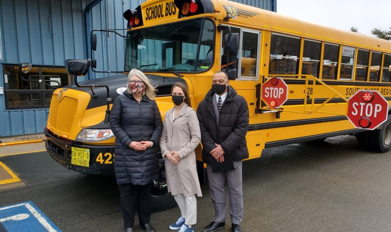 Three people stand in front of a school bus