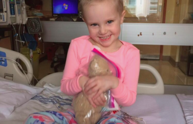 Hayden Foulon sitting in her pajamas and hugging her teddy bear in the hospital.