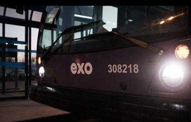 La devanture mauve d'un autobus EXO, les phares allumés, tout près d'un abri-bus au crépuscule.