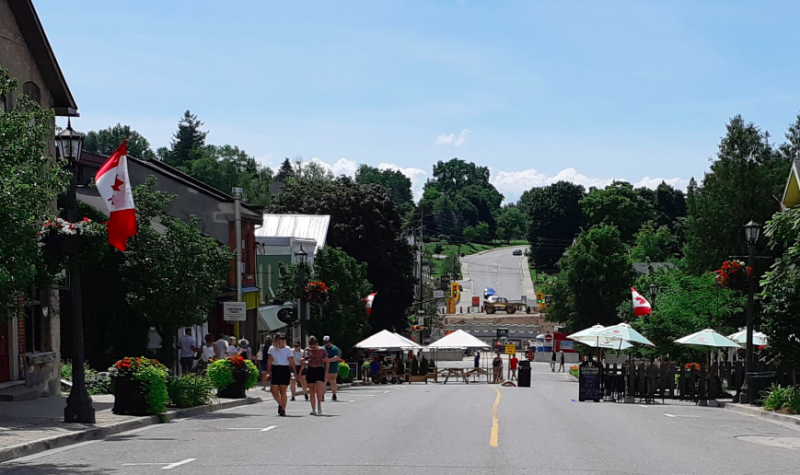 A wide shot of the main street in downtown Elora on a sunny day with tents and vendors seen at a distance
