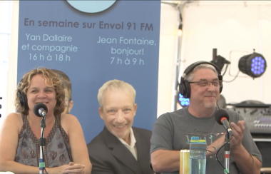 Michèle et Randy tous les deux habillés en gris sont assit devant un micro avec des écouteurs.